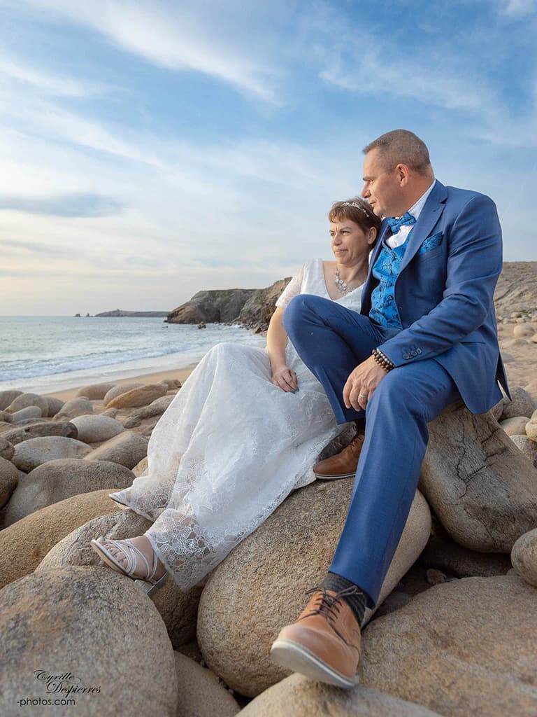 Couple en tenue de mariage assis au bord de la mer